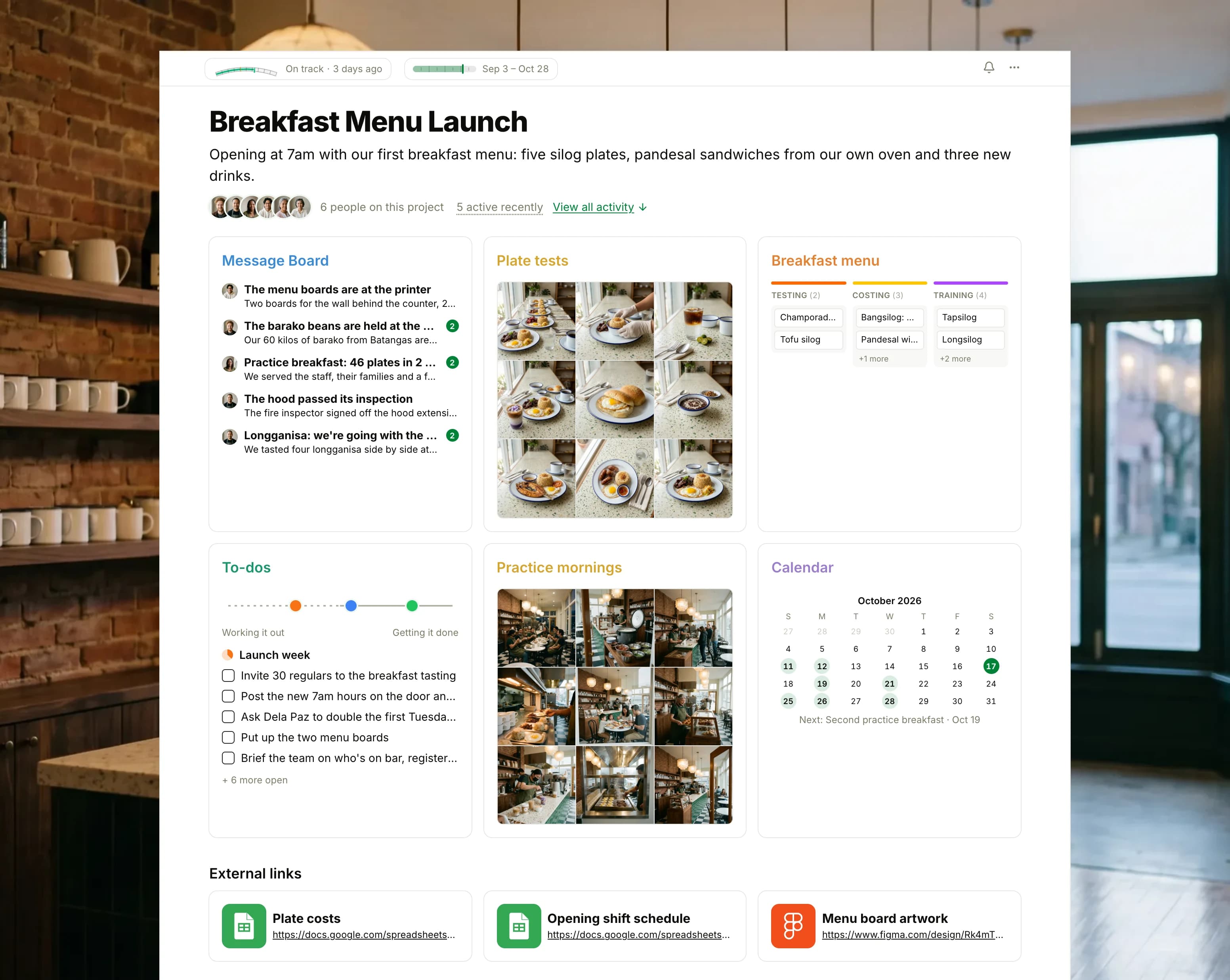 The Breakfast Menu Launch project in Thicket over a photograph of a café counter under capiz shell lamps in the early morning: the health flag reading On track, the launch dates and six people, then six cards: the Message Board with the menu boards at the printer on top, Plate tests as nine photographs of silog plates, pandesal and drinks, the Breakfast menu board with cards in Testing, Costing and Training, To-dos with three lists on the progress chart, Practice mornings as nine photographs of the first practice breakfast, and the Calendar with the second practice breakfast next, with three external links below.