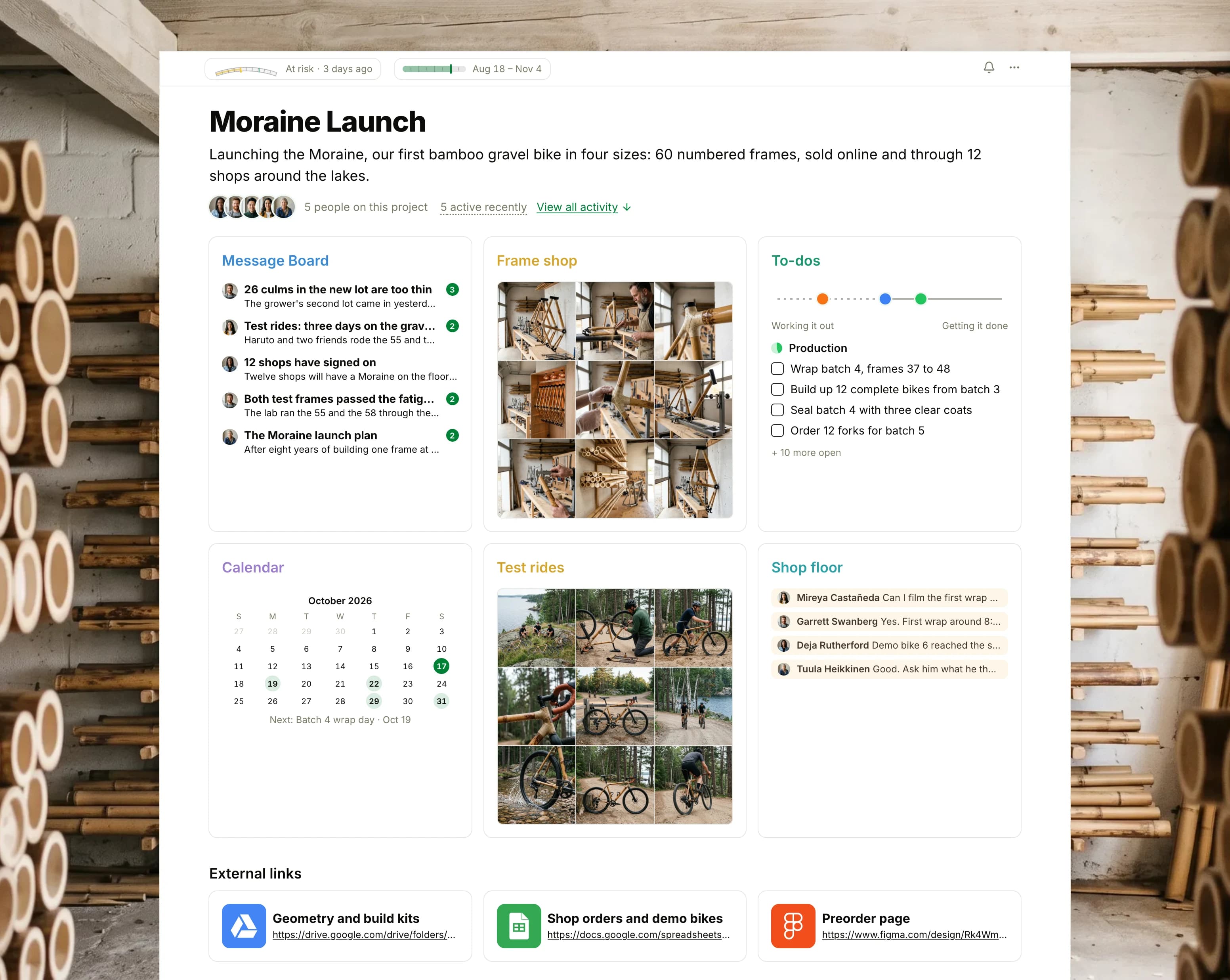 The Moraine Launch project in Thicket over a photograph of cured bamboo poles stacked on a workshop rack: the health flag reading At risk, the launch dates and five people, then six cards: the Message Board with the thin bamboo lot on top, Frame shop as nine photographs of bamboo bike frames being built, To-dos with three lists on the progress chart, the Calendar with batch 4's wrap day, Test rides as nine photographs of the bamboo bike on gravel roads through pine forest, and Chat with the day's builds, then External links to the geometry, the shop orders and the preorder page.