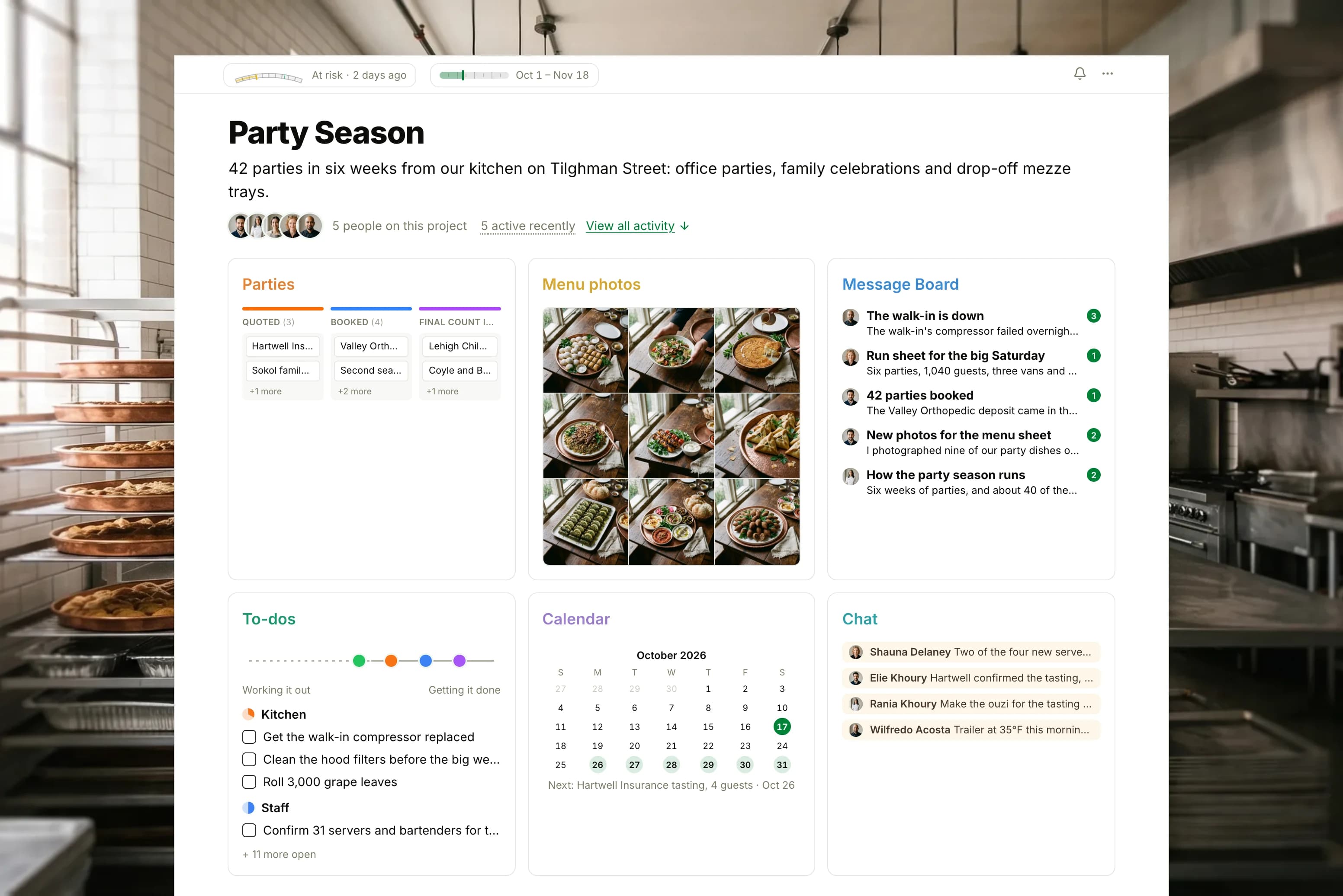 The Party Season project in Thicket over a photograph of a catering kitchen's steel prep tables and copper trays in early light: the health flag reading At risk, the season's dates and five people, then six cards: the Parties board with cards in Inquiries, Quoted, Booked, Final count in and Prep sheet out, Menu photos as nine photographs of the party dishes, the Message Board with the broken walk-in cooler on top, To-dos with four lists on the progress chart, the Calendar with a client tasting next, and Chat about the refrigerated trailer and the morning's baklava.